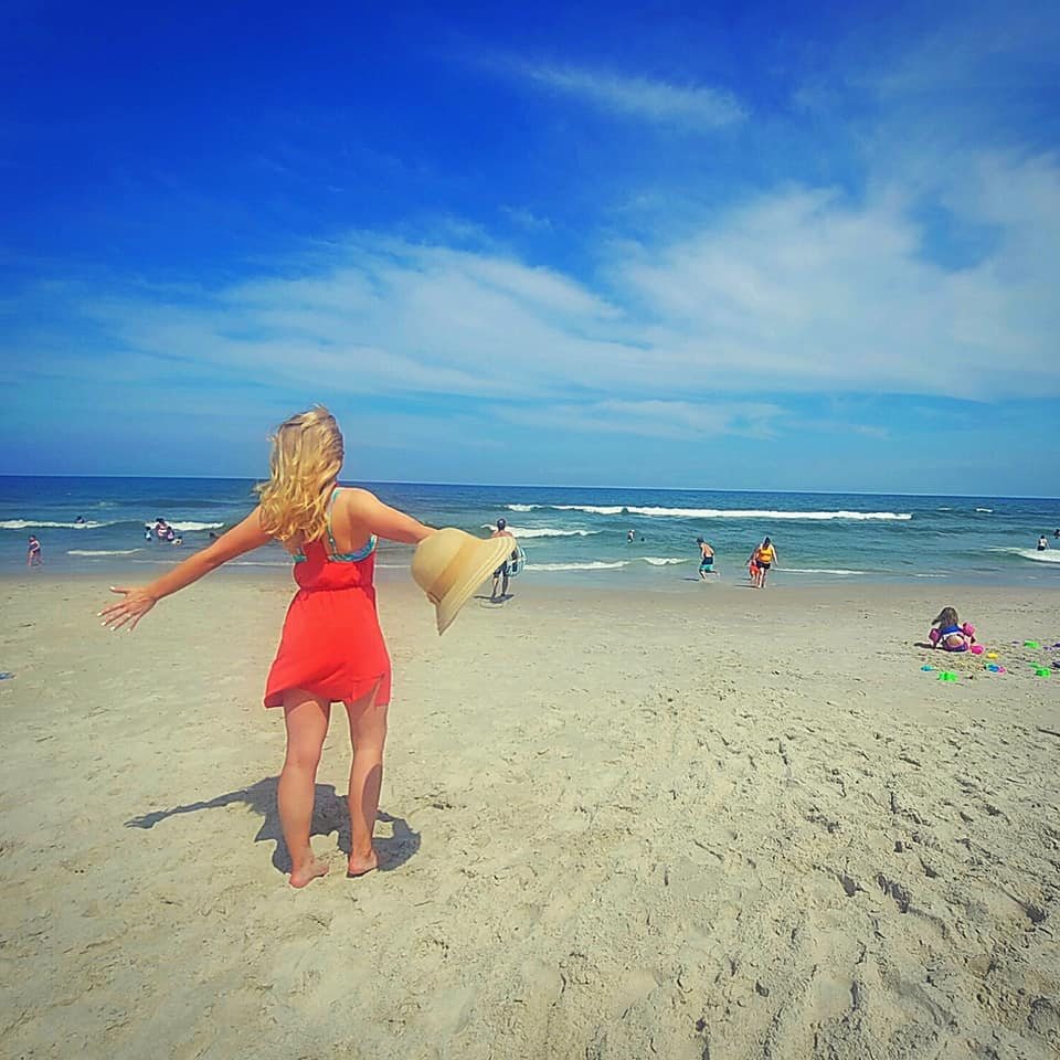 Sarah on the beach in a red dress, arms open